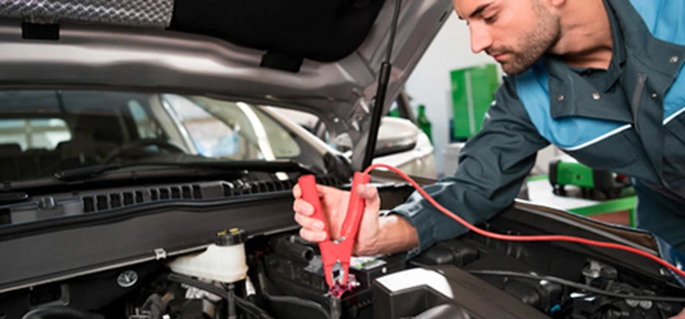 Mechanik podłączający przewód rozruchowy do&nbsp;akumulatora samochodu w&nbsp;warsztacie